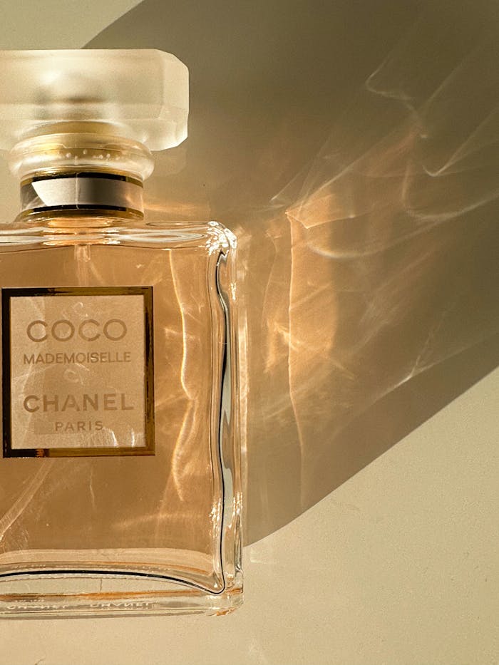 Dlaczego Twoje perfumy pachną krócej niż inne? 5 błędów, które „zabijają” Twój zapach Chanel perfume bottle casting a shadow on a white surface, evoking luxury and elegance.