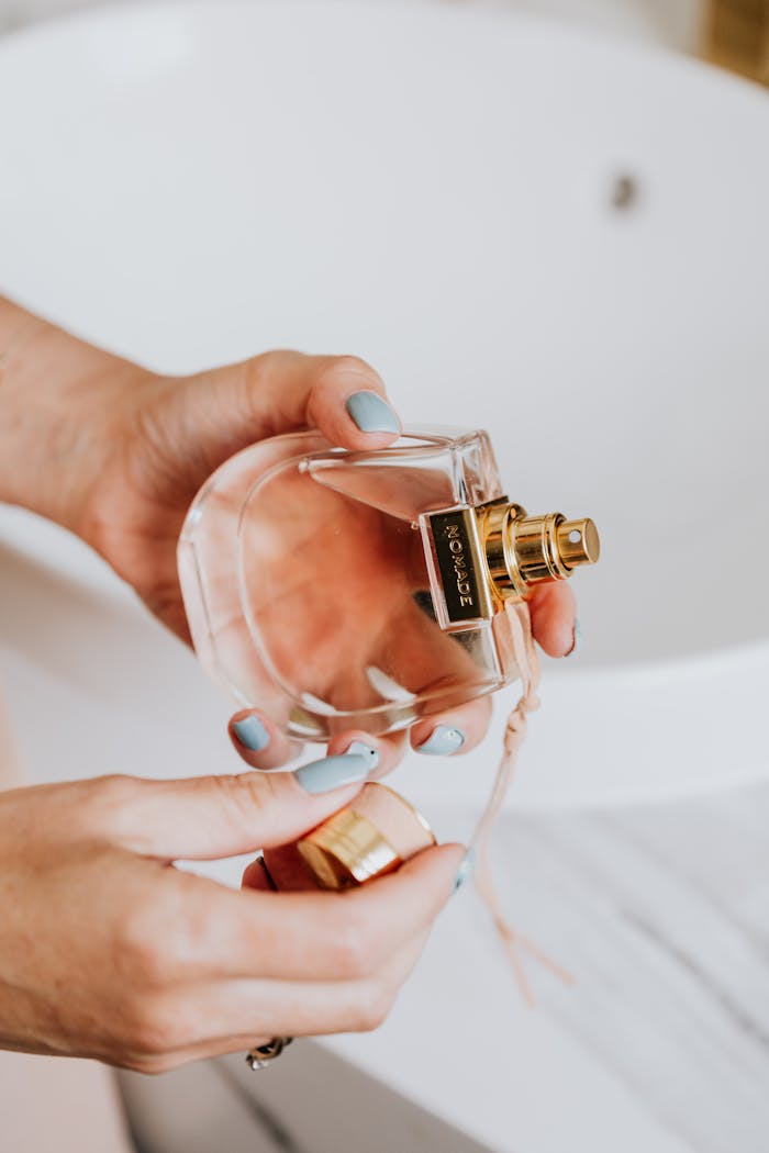 Close-up of a woman's hands holding an elegant perfume bottle inside a brightly lit room.
